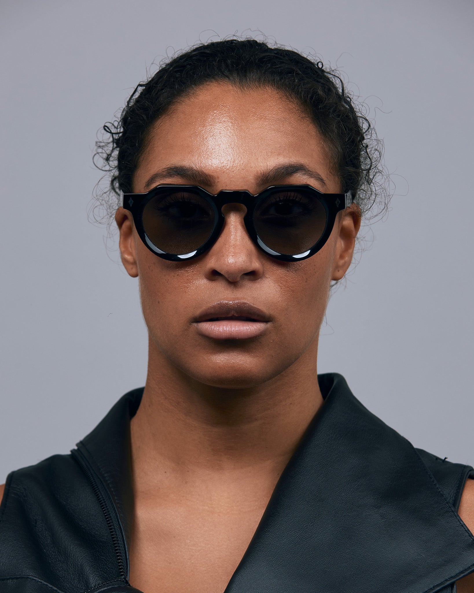 Brutal 2.0 Sunglasses by Tribu Eyewear — Grey grad polarised lens in a black round acetate frame on female grey background.
