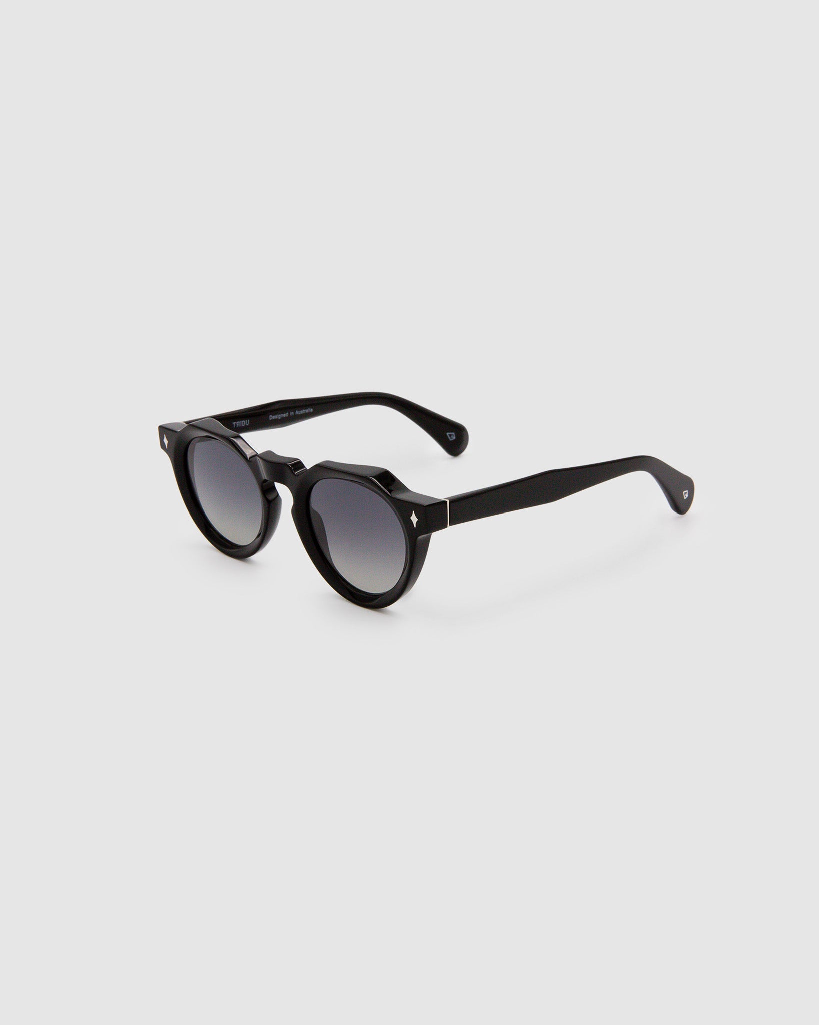 Brutal 2.0 Sunglasses by Tribu Eyewear — Grey grad polarised lens in a black round acetate frame, side view on grey background.