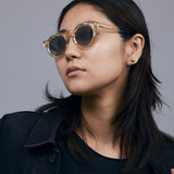 Brutal 2.0 Sunglasses by Tribu Eyewear — Grey grad polarised lens in a Champagne crystal round acetate frame on female model in studio.