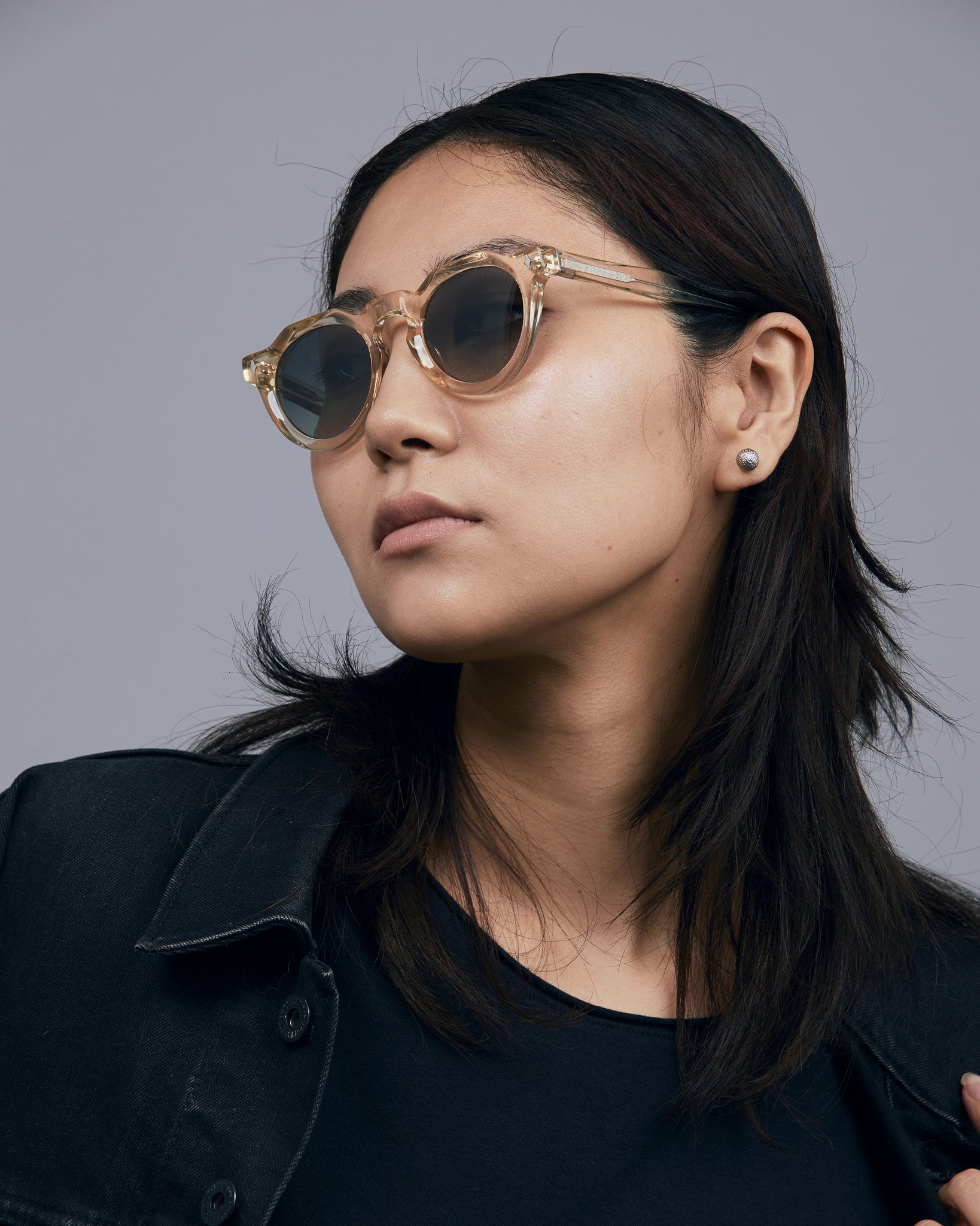 Brutal 2.0 Sunglasses by Tribu Eyewear — Grey grad polarised lens in a Champagne crystal round acetate frame on female model in studio.