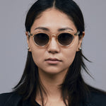 Brutal 2.0 Sunglasses by Tribu Eyewear — Grey grad polarised lens in a Champagne crystal round acetate frame on female model. 
