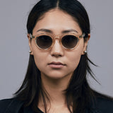 Brutal 2.0 Sunglasses by Tribu Eyewear — Grey grad polarised lens in a Champagne crystal round acetate frame on female model. 
