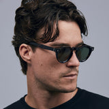 Brutal 2.0 Sunglasses by Tribu Eyewear — Green polarised lens in a round tort acetate frame on a male model.