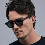 Brutal 2.0 Sunglasses by Tribu Eyewear — Green polarised lens in a round tort acetate frame on a male model grey background.