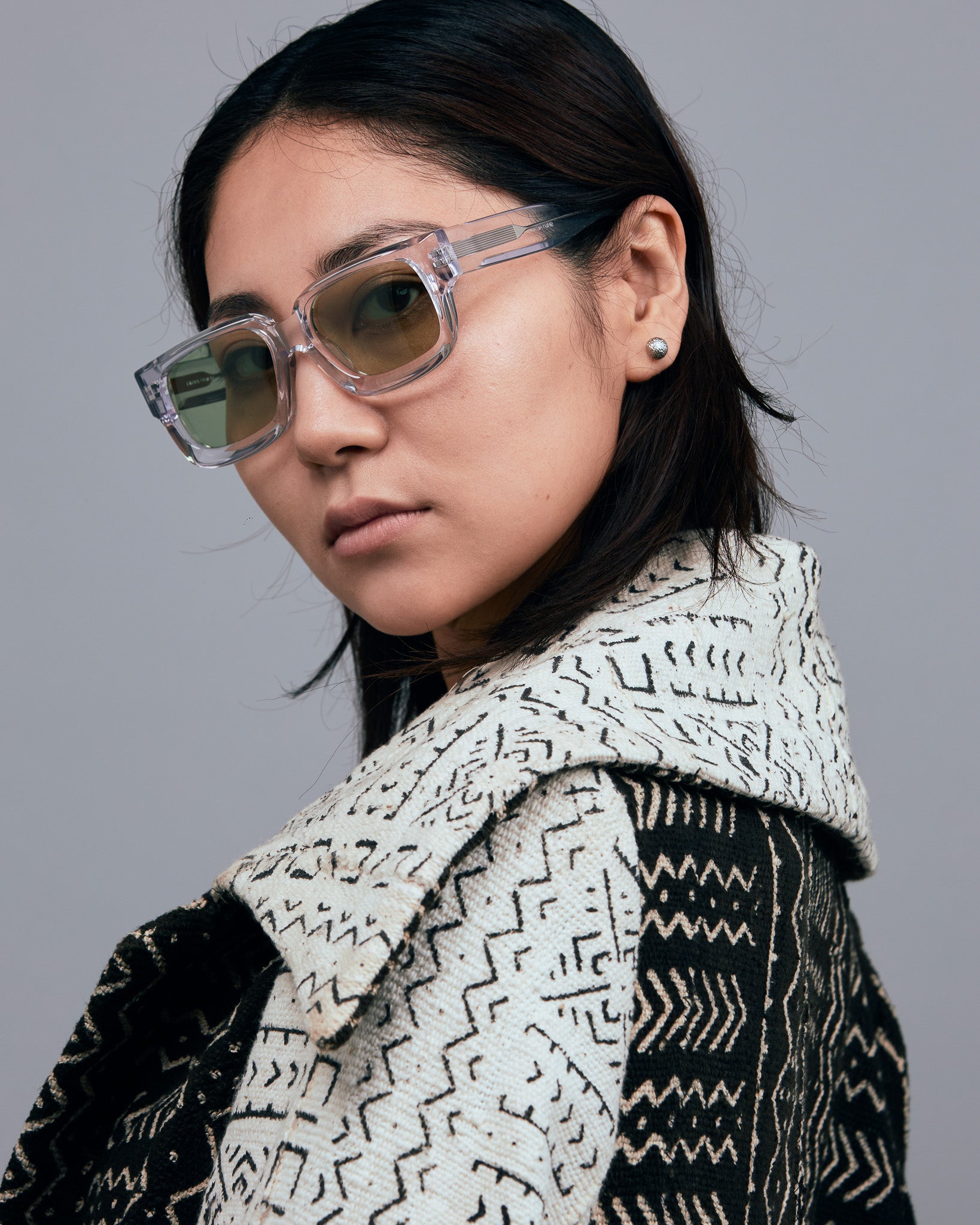 Brutal 3.0  Sunglasses by Tribu Eyewear — Crystal square acetate frame, sage lens, female model light grey background.