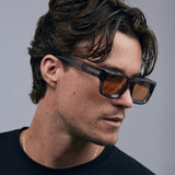 Brutal 3.0  Sunglasses by Tribu Eyewear — Smoke Crystal square acetate frame, desert orange lens, male model light grey background.