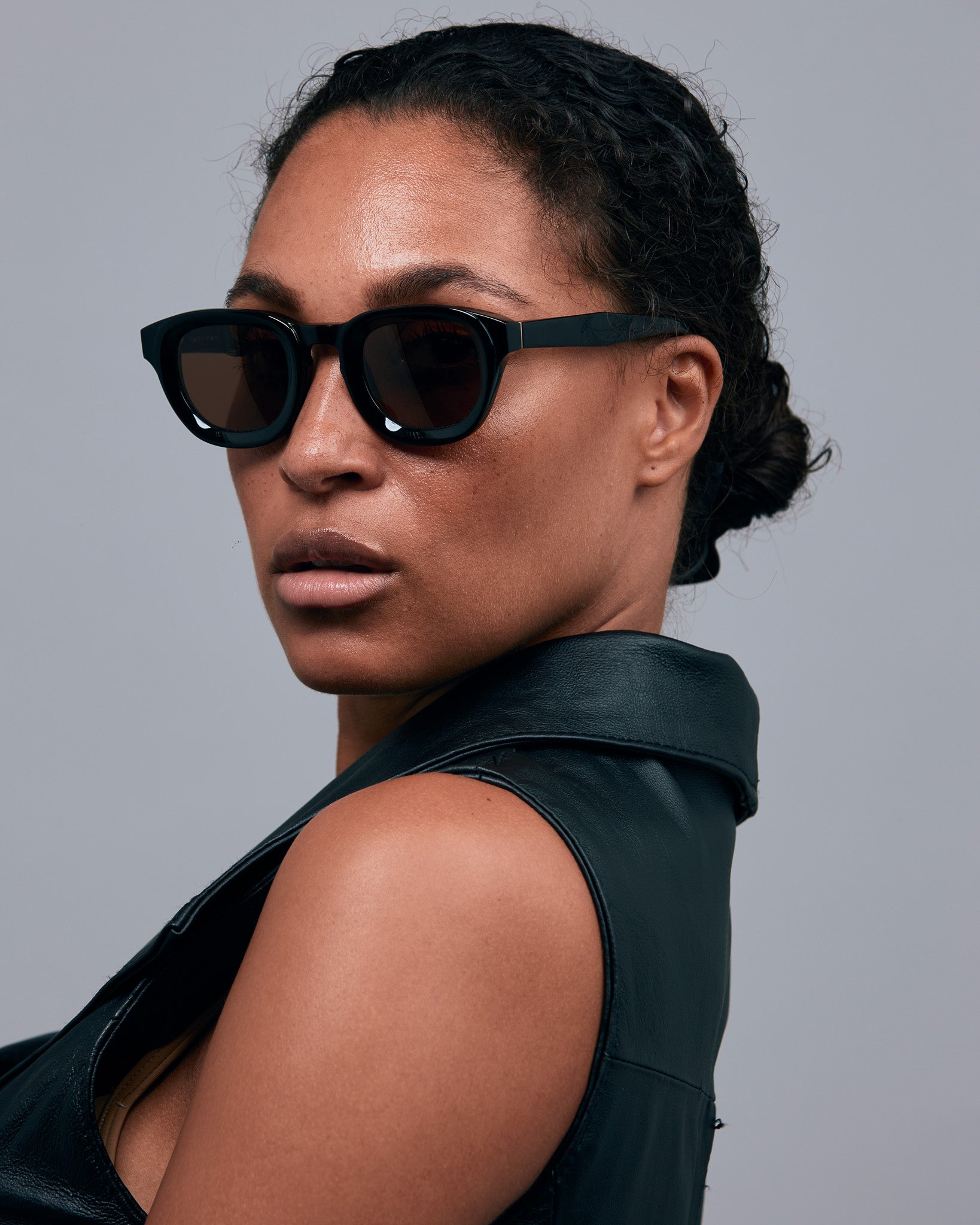 Brutal 4.0 Polarised Sunglasses by Tribu Eyewear — Black Round acetate frame, brown lens, on female light grey background.