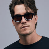 Brutal 4.0 Polarised Sunglasses by Tribu Eyewear — Black Round acetate frame, brown lens, on male light grey background.