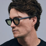 Brutal 4.0 Sunglasses by Tribu Eyewear — Black round acetate frame, sage lens, on male light grey background.