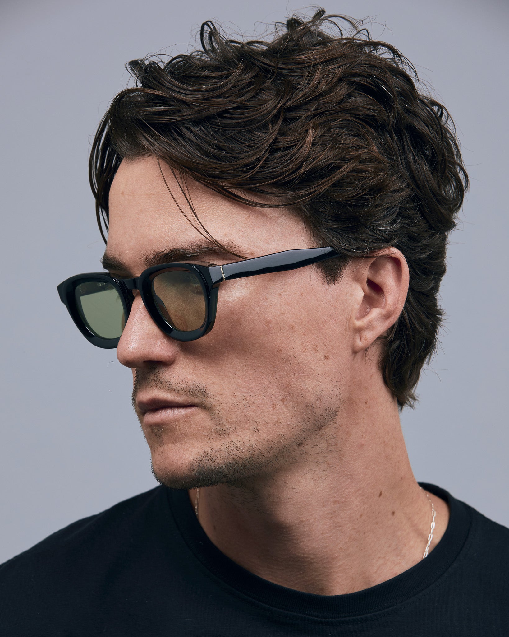 Brutal 4.0 Sunglasses by Tribu Eyewear — Black round acetate frame, sage lens, on male light grey background.