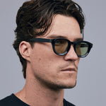 Brutal 4.0 Sunglasses by Tribu Eyewear — Black round acetate frame, sage lens, on male light grey background.