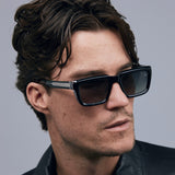 Brutal 5.0 Polarised Sunglasses by Tribu Eyewear — Black on Crystal rectangular acetate frame, grey lens, on male light grey background.