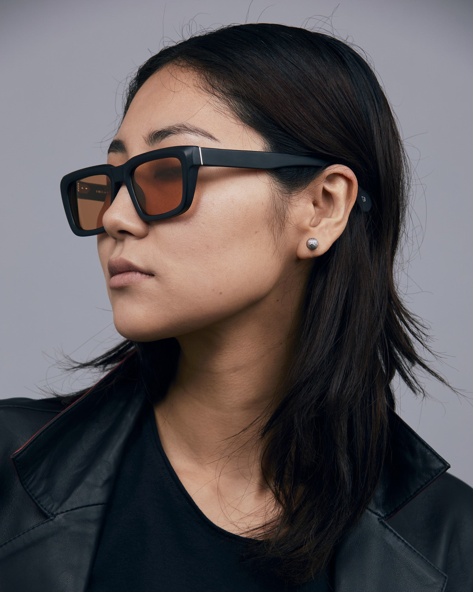 Brutal 5.0 Sunglasses by Tribu Eyewear — Matte black rectangular acetate frame, desert orange lens, on female light grey background.